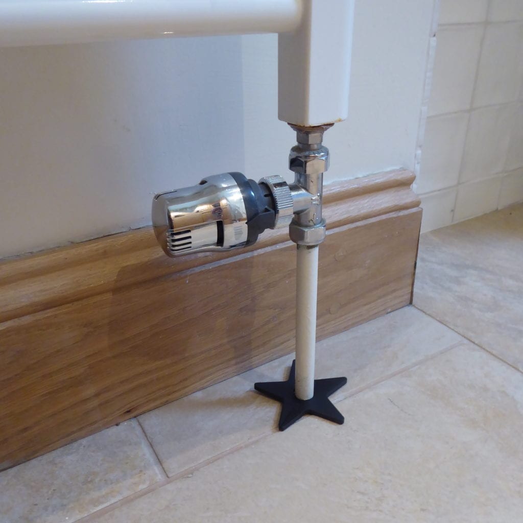 Star-shaped pipe cover on tiled floor around bottom of radiator pipe