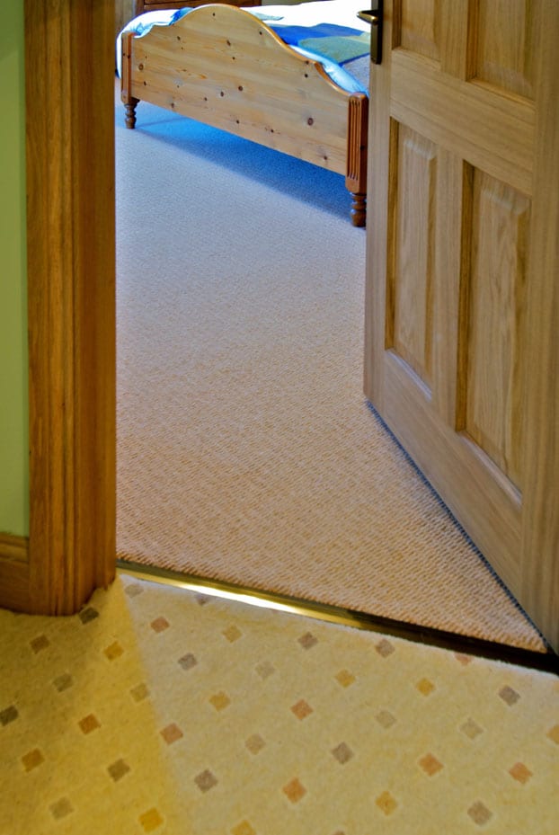 Posh door threshold joins landing to bedroom carpet in doorway, antique brass