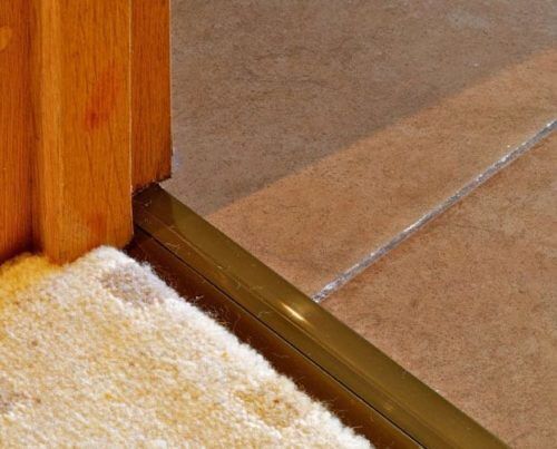 Posh door threshold in antique brass transitioning from tufted carpet to ceramic bathroom floor