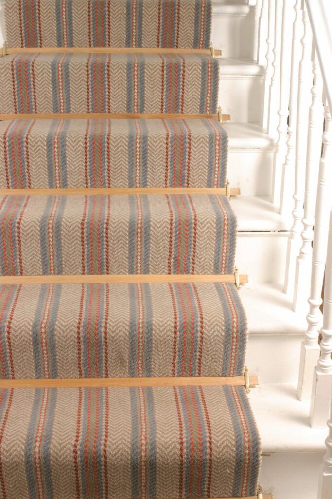 Tudor carpet rods light are a pale oak finish, shown fitted on striped stair runner