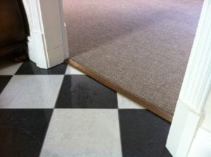 Posh door bar in antique brass joins carpet to LVT flooring in black and white