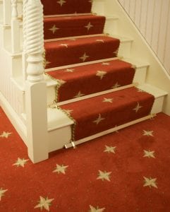 Wooden oak coloured stair rods with metal trim fitted on red stair runner