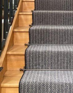 Balladeer stair rod design in antique bronze on grey striped runner stair carpet with wrought iron bannister