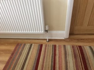 Circular design pipe cover around radiator pipe, striped rug