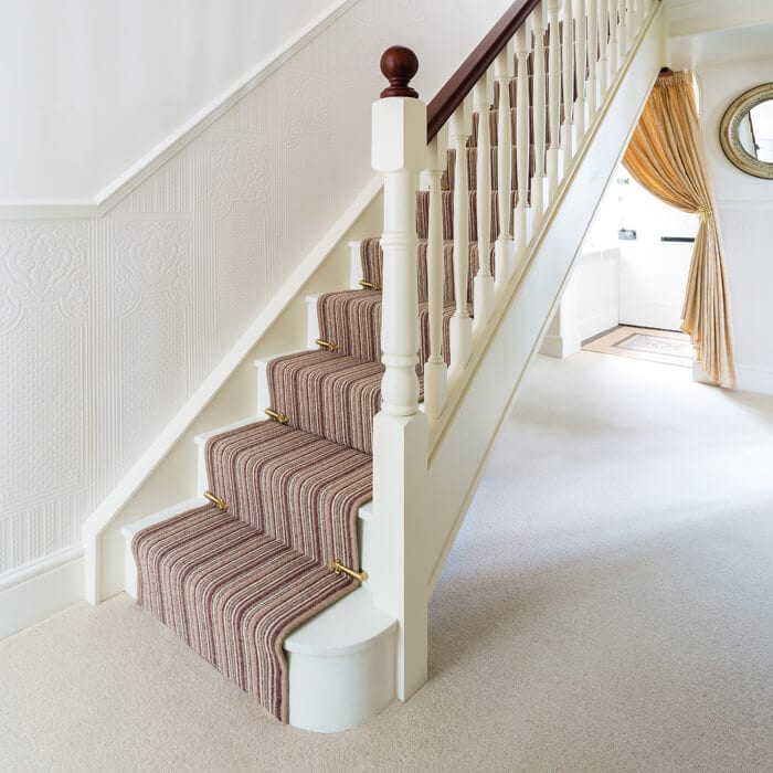 Polished brass stair clips fitted to stair runner on striped carpet